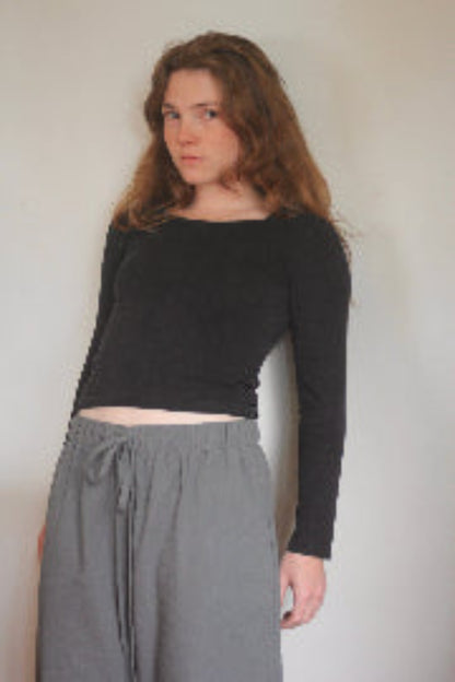 Woman wearing a black long-sleeve top and gray pants against a plain background